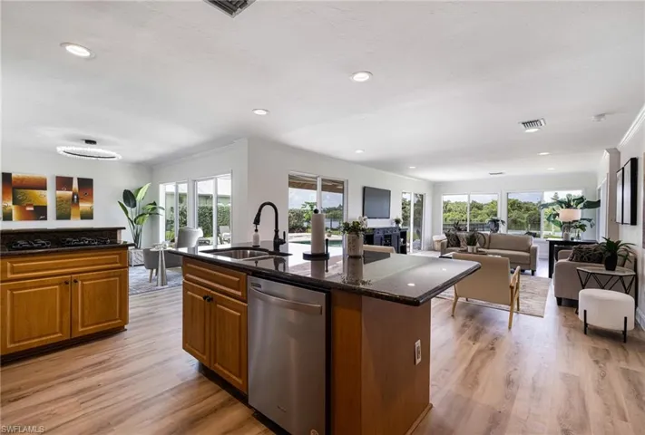 Kitchen with brown cabinets, open floor plan, stainless steel dishwasher, dark stone counters, and recessed lighting