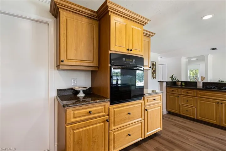 Kitchen with dark stone countertops, black oven, dark wood-style floors, recessed lighting, and brown cabinetry