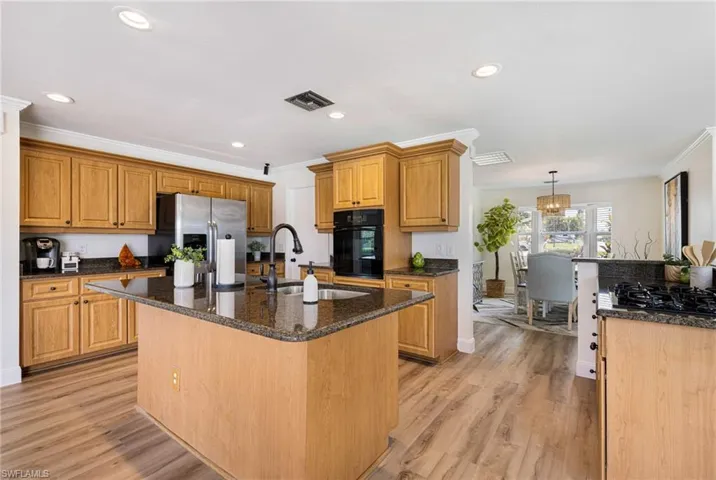 Kitchen featuring a center island with sink, crown molding, stainless steel fridge with ice dispenser, dark stone countertops, and brown cabinetry