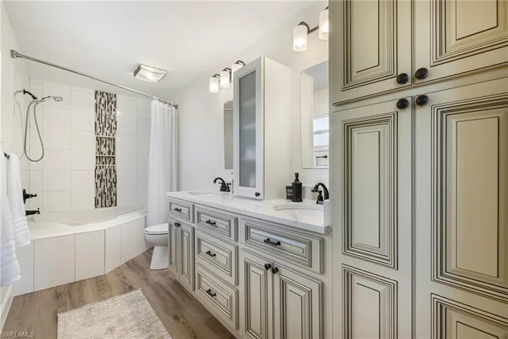 Bathroom with tiled shower / bath combo, light wood-style flooring, and double vanity