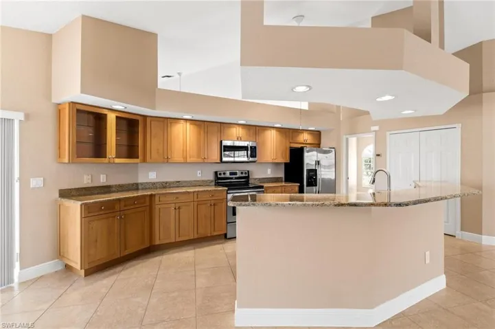 Kitchen with high vaulted ceiling, stone counters, appliances with stainless steel finishes, brown cabinetry, and glass insert cabinets