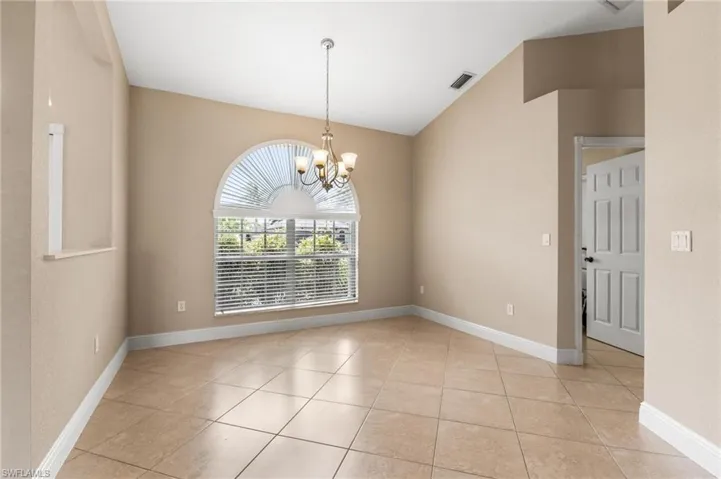 Empty room featuring baseboards, visible vents, vaulted ceiling, and an inviting chandelier