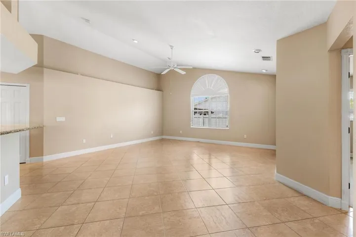Empty room featuring light tile patterned flooring, visible vents, baseboards, ceiling fan, and vaulted ceiling