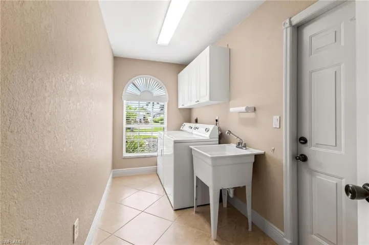 Washroom with a textured wall, light tile patterned flooring, cabinet space, and baseboards