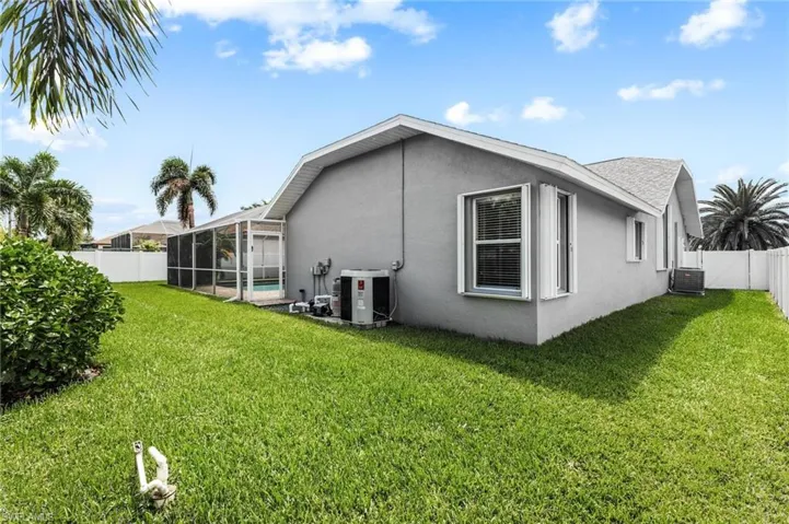 Back of property featuring stucco siding, a fenced backyard, central AC unit, glass enclosure, and a lawn