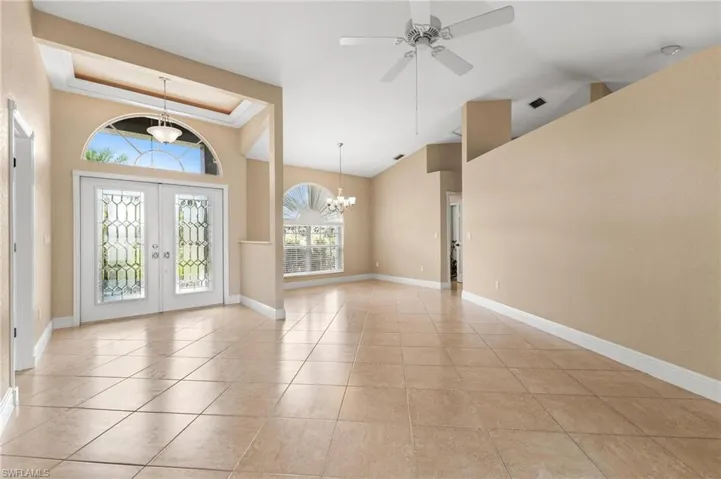 Entrance foyer with french doors, ceiling fan with notable chandelier, baseboards, a raised ceiling, and light tile patterned flooring