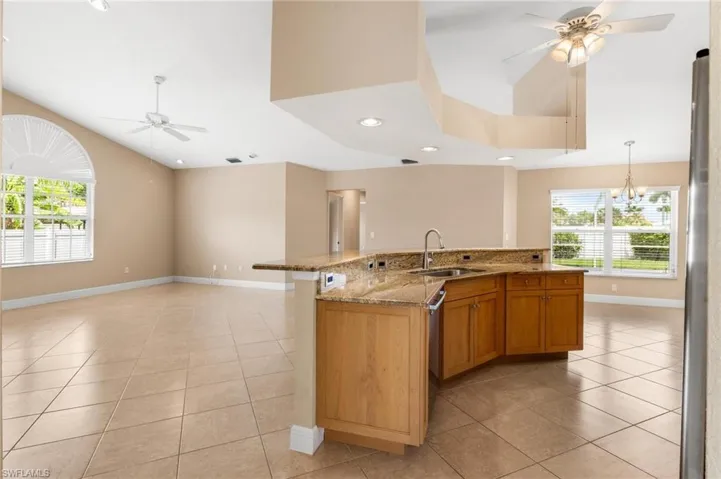 Kitchen featuring ceiling fan with notable chandelier, a wealth of natural light, light stone countertops, and a sink