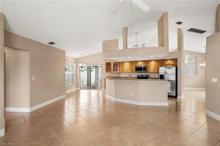 Kitchen featuring light tile patterned floors, stainless steel appliances, ceiling fan with notable chandelier, and brown cabinets