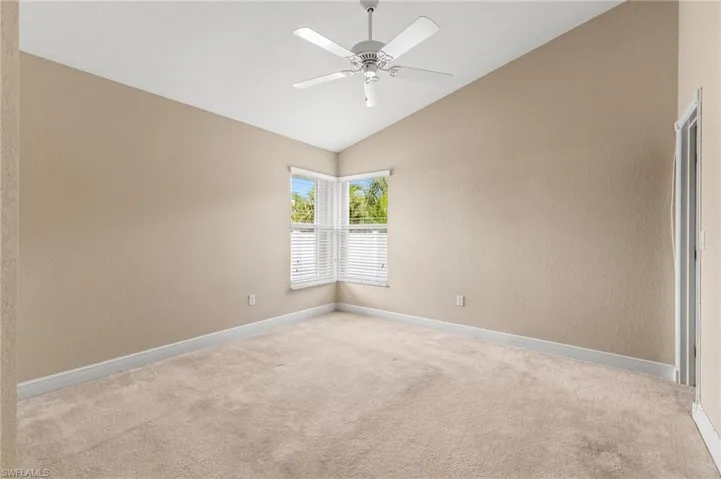 Carpeted spare room with a ceiling fan, a textured wall, baseboards, and vaulted ceiling