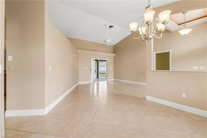 Unfurnished room with vaulted ceiling, light tile patterned floors, ceiling fan with notable chandelier, baseboards, and visible vents
