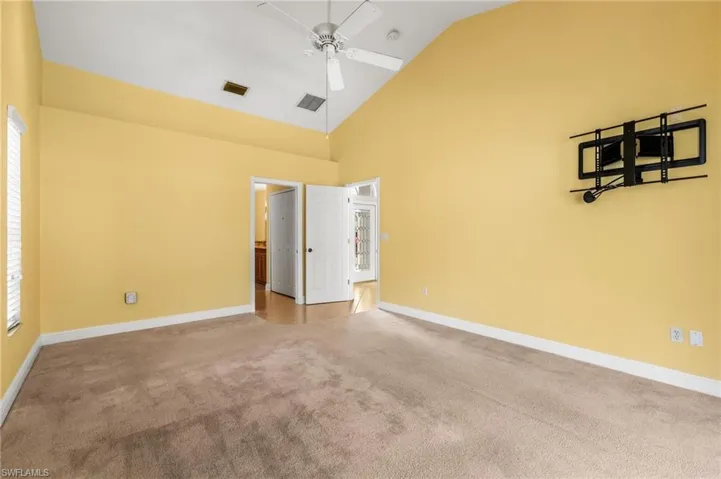 Carpeted empty room with high vaulted ceiling, visible vents, baseboards, ceiling fan, and a wealth of natural light