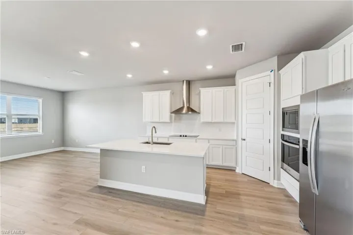 Kitchen with tasteful backsplash, white cabinets, a kitchen island with sink, stainless steel appliances, and wall chimney range hood