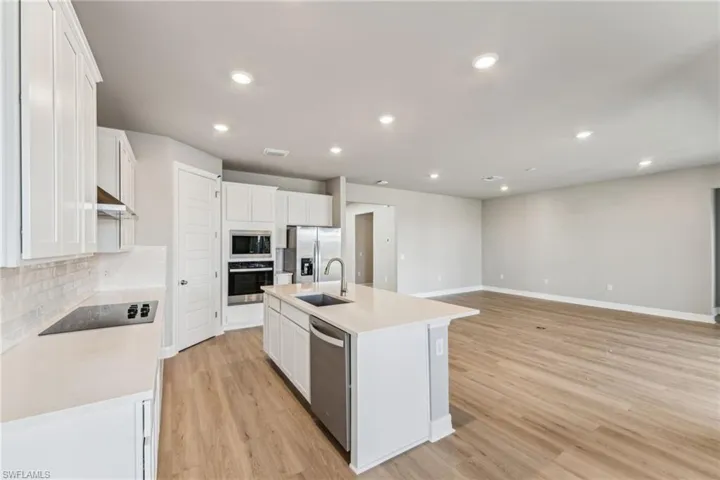 Kitchen featuring an island with sink, white cabinetry, sink, backsplash, and stainless steel appliances