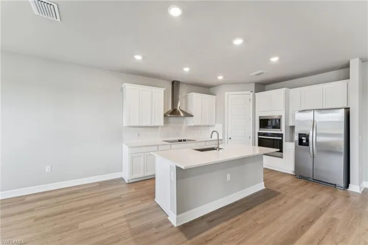 Kitchen featuring white cabinetry, an island with sink, sink, stainless steel appliances, and wall chimney exhaust hood