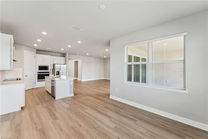Kitchen featuring appliances with stainless steel finishes, white cabinets, decorative backsplash, a kitchen island with sink, and light wood-type flooring