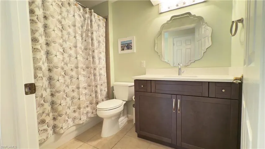Full bathroom with newer vanity, toilet, tile patterned flooring, and curtained shower over tub