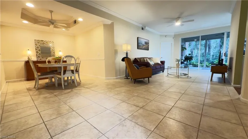 Spacious open living area with light tile patterned flooring, fan, and ornamental molding