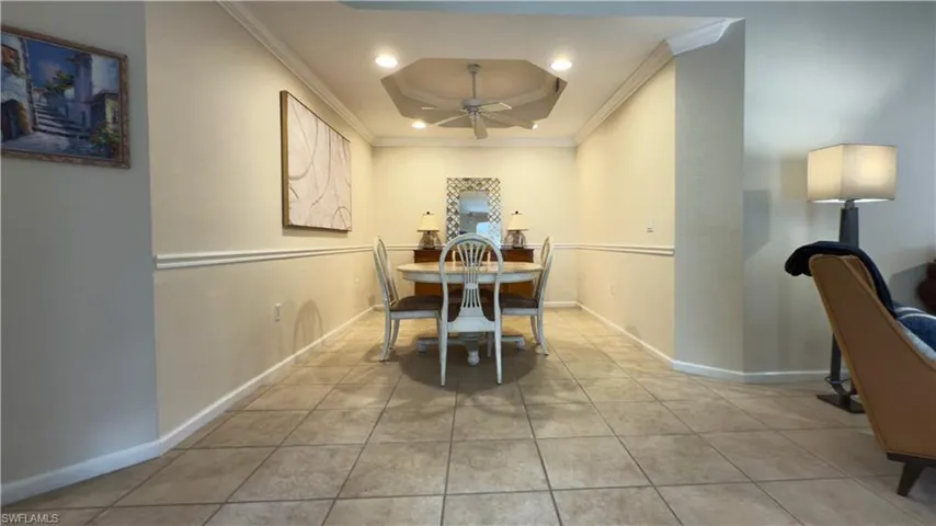 Tiled dining space with a tray ceiling, ceiling fan, and crown molding