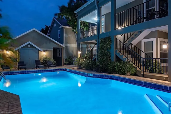Pool at twilight with a balcony, stairway, a patio area, an outdoor pool, and an outdoor structure