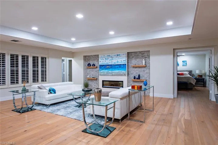 Living room featuring a tray ceiling, light wood-type flooring, recessed lighting, and a large fireplace