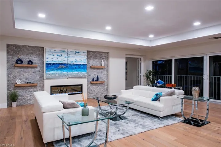 Living room with light wood-type flooring, a raised ceiling, a glass covered fireplace, and recessed lighting