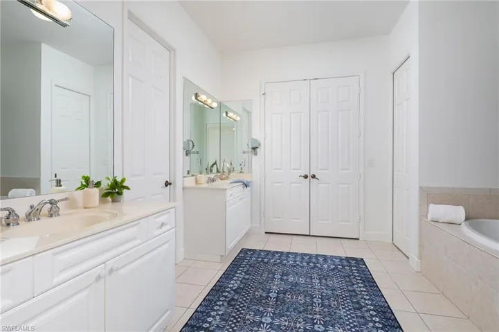Bathroom featuring a closet, light tile patterned floors, two vanities, and tiled bath
