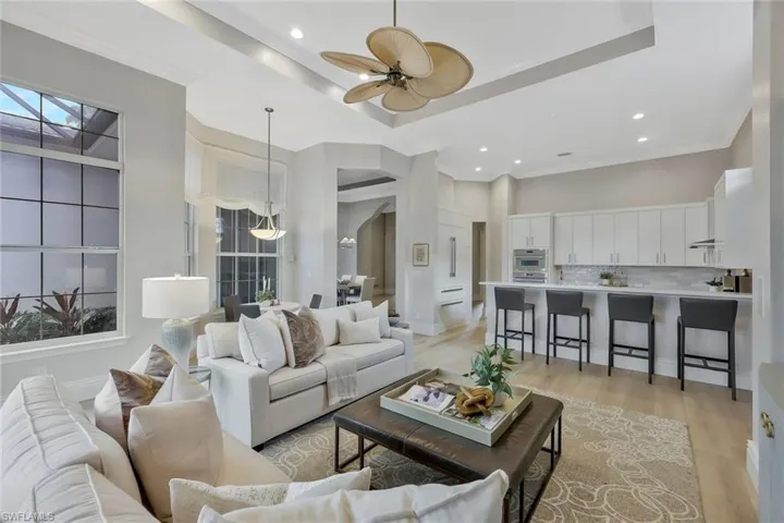 Living area featuring a tray ceiling, light wood-style floors, a ceiling fan, ornamental molding, and recessed lighting