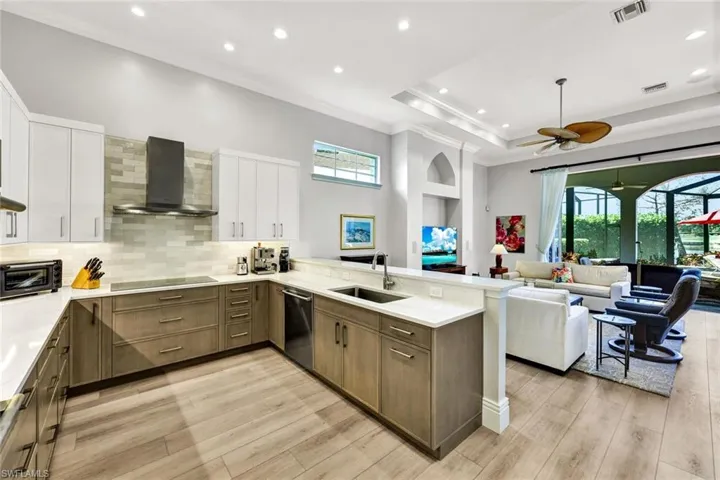 Kitchen featuring a peninsula, wall chimney range hood, open floor plan, backsplash, and crown molding