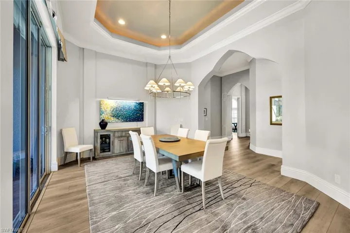 Dining area with a tray ceiling, ornamental molding, wood finished floors, arched walkways, and a chandelier