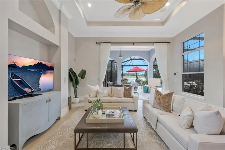 Living room featuring a tray ceiling, a sunroom, crown molding, a ceiling fan, and recessed lighting