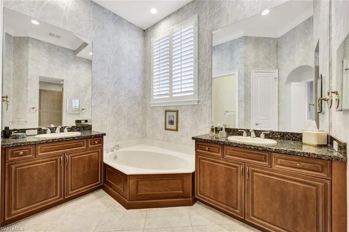 Bathroom with a bath, light tile patterned flooring, two vanities, ornamental molding, and recessed lighting