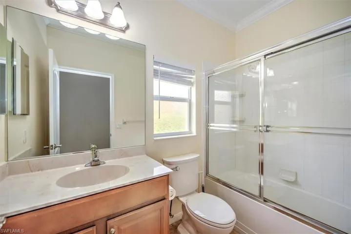 Full bathroom featuring combined bath / shower with glass door, oversized vanity, toilet, and crown molding