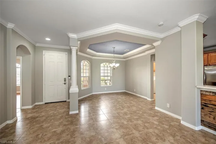 Tiled foyer entrance featuring ornate columns, a chandelier, a raised ceiling, and ornamental molding