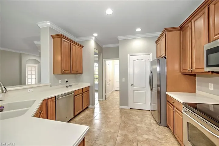 Kitchen featuring ornamental molding, light tile floors, sink, and appliances with stainless steel finishes