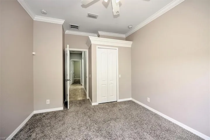 Unfurnished bedroom featuring ceiling fan, a closet, carpet flooring, and ornamental molding