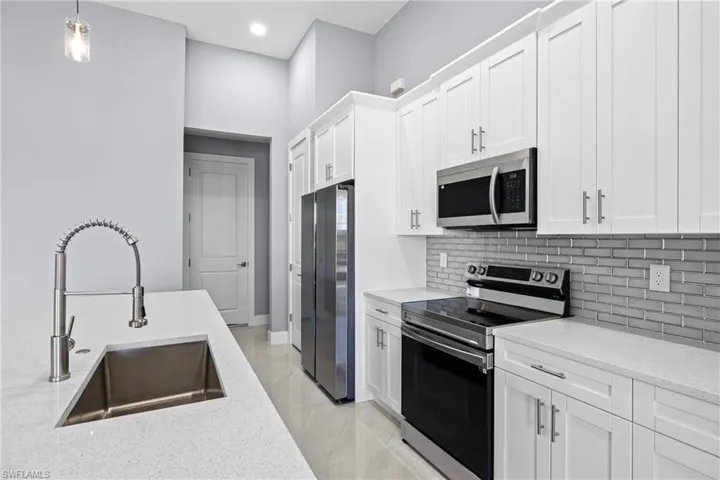Kitchen featuring hanging light fixtures, tasteful backsplash, white cabinetry, appliances with stainless steel finishes, and sink