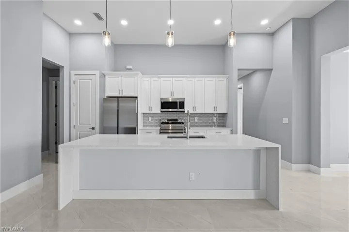 Kitchen with a high ceiling, an island with sink, sink, and appliances with stainless steel finishes