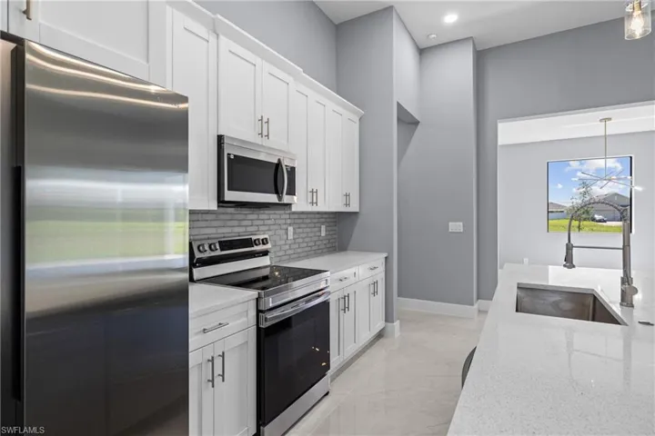 Kitchen featuring light tile flooring, backsplash, hanging light fixtures, appliances with stainless steel finishes, and sink