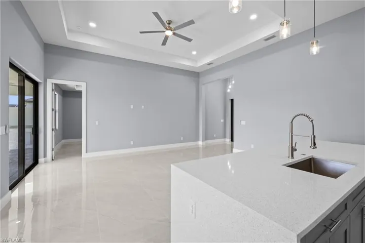 Kitchen featuring decorative light fixtures, sink, light stone countertops, and a raised ceiling