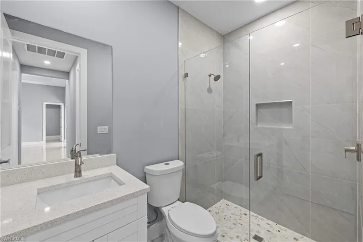Bathroom featuring a shower with shower door, vanity, and toilet