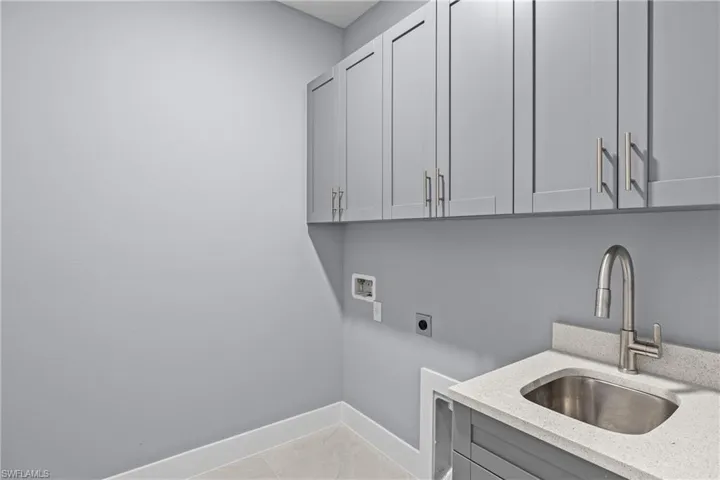 Clothes washing area featuring washer hookup, electric dryer hookup, light tile floors, sink, and cabinets