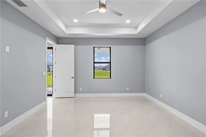 Tiled empty room with ceiling fan and a raised ceiling
