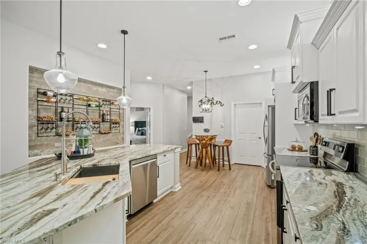 Kitchen with appliances with stainless steel finishes, decorative backsplash, white cabinetry, light wood-style flooring, and recessed lighting