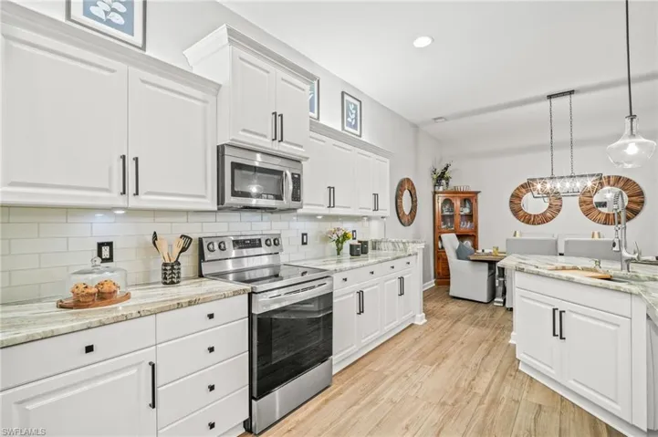 Kitchen featuring stainless steel appliances, decorative backsplash, light wood-type flooring, white cabinetry, and recessed lighting