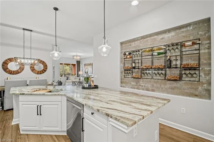 Kitchen featuring stainless steel dishwasher, a chandelier, white cabinets, and light stone counters