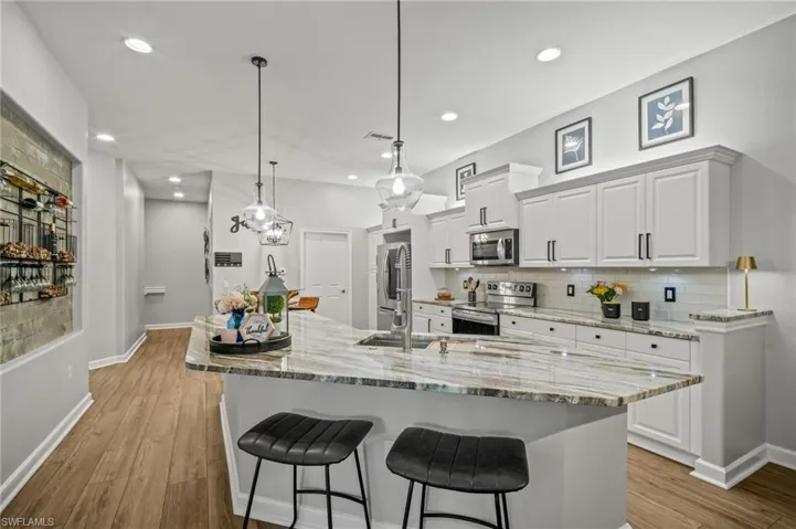 Kitchen featuring appliances with stainless steel finishes, a breakfast bar area, decorative backsplash, white cabinets, and light wood-style floors