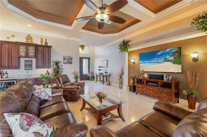 Living room featuring coffered ceiling, a ceiling fan, ornamental molding, bar with sink, and beamed ceiling