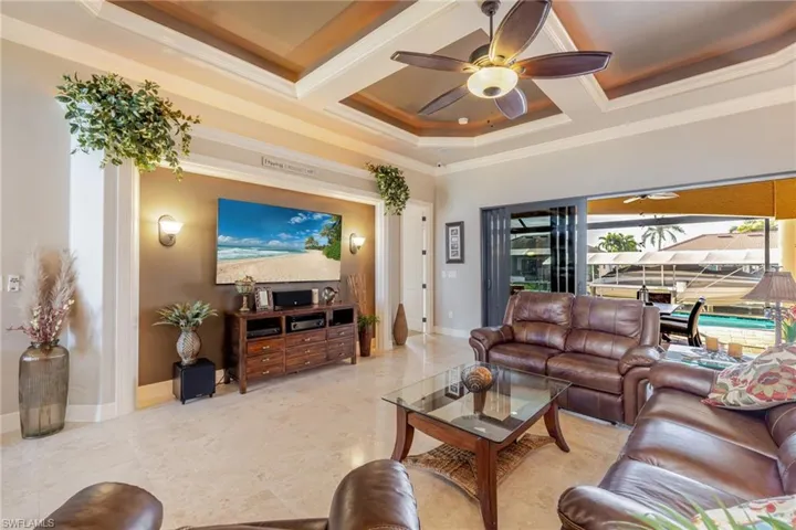 Living room with a ceiling fan, coffered ceiling, ornamental molding, and beam ceiling