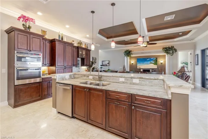 Kitchen featuring ornamental molding, decorative light fixtures, light stone counters, coffered ceiling, and ceiling fan