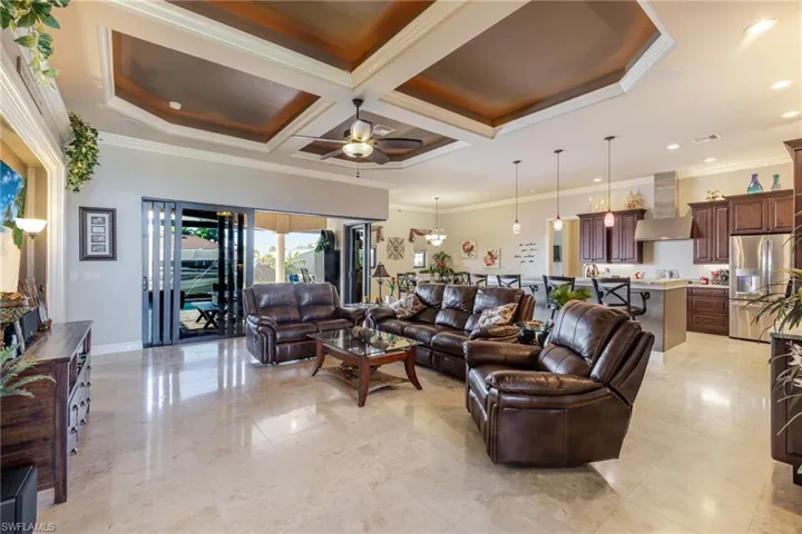Living room with ornamental molding, a ceiling fan, coffered ceiling, beam ceiling, and a chandelier